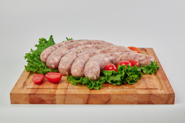 Meat kupatas five pieces with red cherry tomatoes and green lettuce leaves on a rectangular wooden cutting board on a white background.