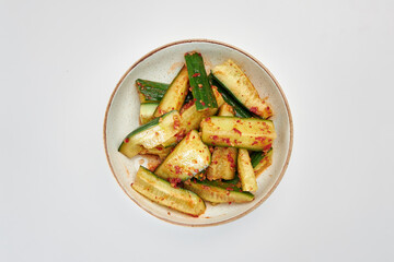 Fresh sliced cucumbers, sprinkled with red hot pepper and vegetable oil in a round white plate on a white background.