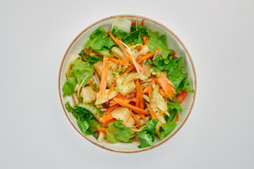 Salad of fresh Peking cabbage, carrots, celery, yellow raisins, green salad, seasoned with vegetable oil in a round white plate on a white background.