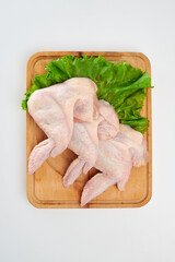 Three fresh chicken wings with green lettuce leaves on a rectangular wooden cutting board on a white background.
