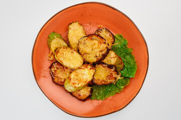 Baked eleven slices of zucchini and eggplant skinned with cheese, garlic, and lettuce in a round orange plate on a white background.