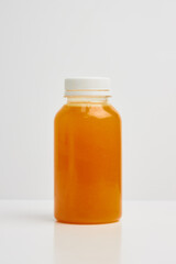 Transparent plastic bottle with a white lid, with orange juice inside on a white background.