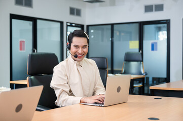 Smile operator asian gay agent with headset working with laptop on customer consultation in the...