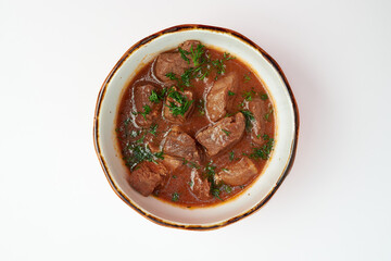 Meat goulash with broth, sprinkled with chopped fresh dill in a white round plate on a white...