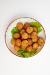 Breaded cheese balls with three green lettuce leaves in a white round plate on a white background.