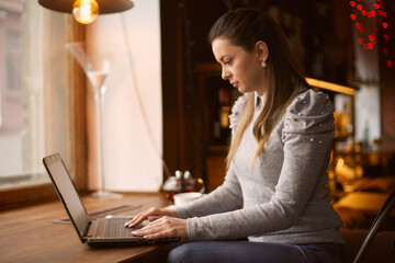 Young girl works in a cafe on a laptop performs customer work remotely.