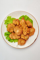 Pieces of chicken fillet, baked in batter, sprinkled with finely chopped dill, with three green lettuce leaves in a round white plate on a white background.