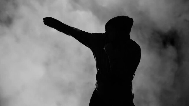 Silhouetted shot: a boxer training alone, wearing a hoodie, under a background of rising gray smoke.
