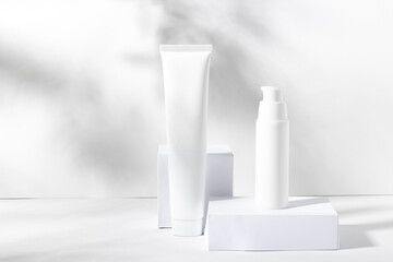 A set of white cosmetic jars on square stands with shadows. Toothpaste, face and body cream, hair shampoo. Professional cosmetics for skin care. Organic cosmetics.