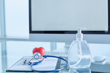 Doctor's office. On a glass table there is a computer, a keyboard dispenser, a stethoscope, a...
