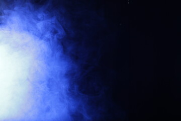 Artificial smoke in blue light on black background
