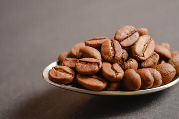 Macro photography  shot of Roasted coffee beans served in silver vintage stainless steel spoon on dark background. High quality organic aroma seeds. Copy space text image

