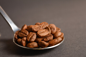 Macro shot of Roasted coffee beans served in silver vintage stainless steel spoon on dark background. High quality organic aroma seeds. Copy space text image
