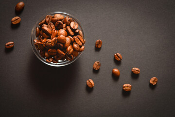 Top view of Roasted coffee beans in bowl with scattered seeds on dark background. High quality organic aroma seeds. Copy space text image
