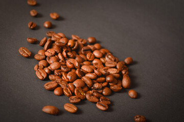 Side view of roasted coffee beans Handful. High quality organic arabica seeds. Coffee beans scattered on dark background out of focus. Copy space text image

