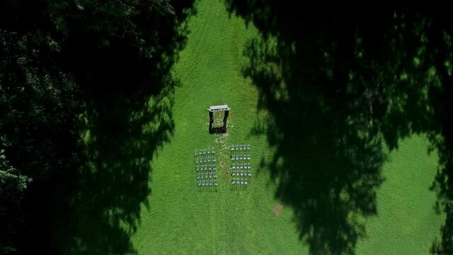 Wedding exit ceremony on the lawn near the forest. Wedding white decor arch chairs for guests in a clearing near the trees. Wedding on the green field on a sunny summer day. Drone areal view shot