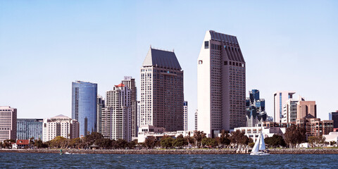 downtown San Diego California skyline showing skyscrapers, hotels and the Embarcadero Marina Park with the San Diego Bay and a single sailboat in the foreground