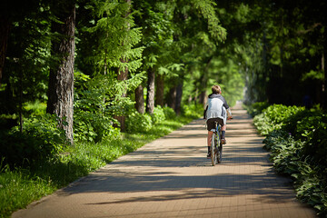 Man rides a bicycle on a road in a green park on a sunny summer day.