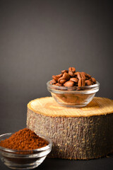 Roasted coffee beans served in glass bowl on wooden log, dark background. High quality organic aroma seeds. Ground coffee in bowl out of focus. Copy space text image
