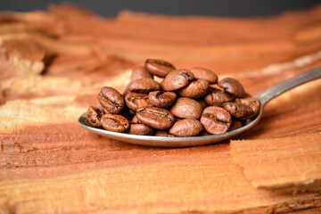 Close up to Roasted coffee beans served in silver vintage spoon on wooden log with Dark background....