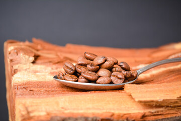 Side view of Roasted coffee beans served in silver vintage spoon on wooden log with Dark...