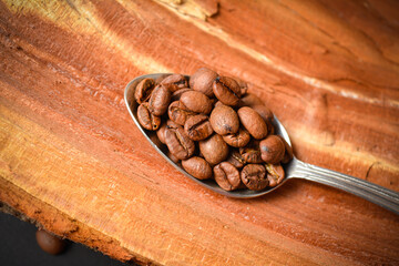 Top view of Roasted coffee beans served in silver vintage spoon on wooden log background. Creative...