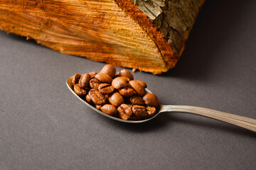 Side view of Roasted coffee beans served in silver vintage spoon with wooden log on Dark...