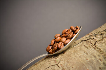 Roasted coffee beans served in silver vintage spoon on wooden log. Dark background. Creative eco...