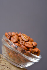 Vertical image of whole coffee beans served in glass bowl on wooden log with dark background. High quality organic arabica Roasted coffee seeds. Copy space text image
