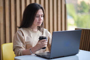 happy woman using laptop while sitting at cafe. Girl browsing internet, chatting, blogging. Brunette studying on laptop and enjoying coffee