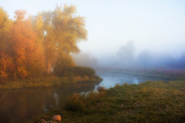 Bright sunny but still foggy morning on the river with an autumn landscape