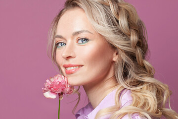 Happy pretty blonde woman with flower smiling on pink, beautiful face close up