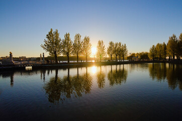 Scenic sunset landscape near embankment in the Taras Shevchenko Park in Ternopil. Sun and trees reflected in the tranquil water. Famous touristic place and romantic travel destination. Ukraine