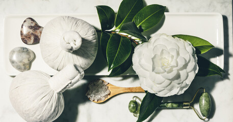 Flat lay composition with spring camelia flower and various beauty care products on white marble table