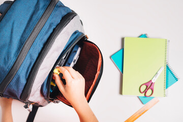 View from above of a child's hand taking a marker from his school bag. Notebooks and rulers on the table. Back to school concept