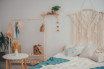 The concept of home comfort. Bed, knitted panel, wooden shelf with wooden toys, wooden clothes hanger. Scandi style.
