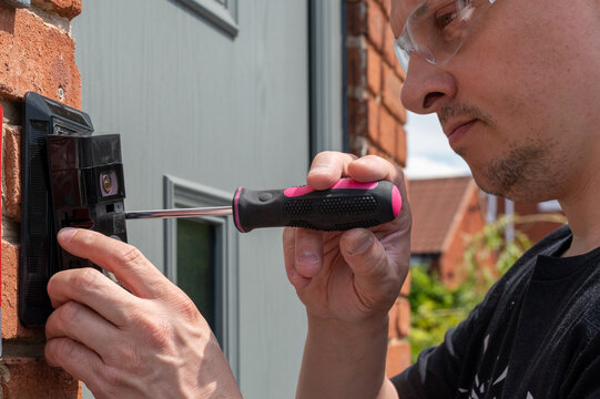 Man Installing A Smart Doorbell With Security Camera And Solar Charger Next To The Front Door Of His House