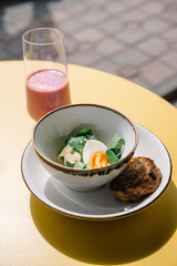 cold beet soup with kefir, fresh herbs, boiled egg and slice of grilled bread on the table of cafe summer terrace
