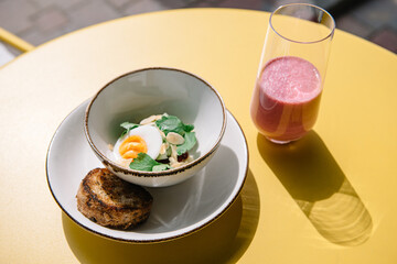 cold beet soup with kefir, fresh herbs, boiled egg and slice of grilled bread on the table of cafe summer terrace