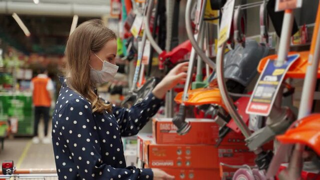 Young woman in a medical mask came to the garden tools store to buy a lawn mower