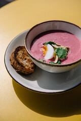 cold beet soup with kefir, fresh herbs, boiled egg and slice of grilled bread on the table of cafe summer terrace