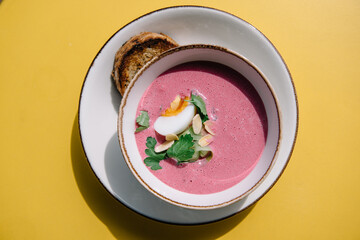 cold beet soup with kefir, fresh herbs, boiled egg and slice of grilled bread on the table of cafe summer terrace
