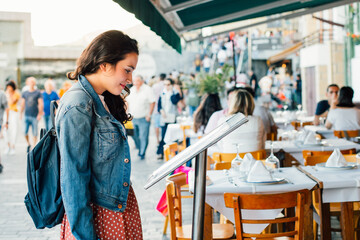 Naklejka premium Young tourist woman choosing a restaurant with terrace for dinner