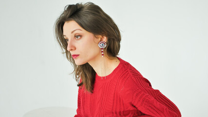 Studio portrait of young woman in red knitted sweater and earring on white background