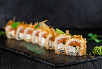 Japanese sushi roll on Black slate stone plate on wooden background. sushi pieces with salmon, cucumber, Tofu cheese, spring onion scallions wrapped in rice with tuna chips Bonito on top with greens
