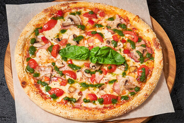 Traditional Italian uncut whole meat pizza with bacon, tomatoes, mozzarella cheese, mushrooms. Pizza served with fresh basil leaf, pesto sauce. Dish on parchment paper, wooden board. Rustic Food
