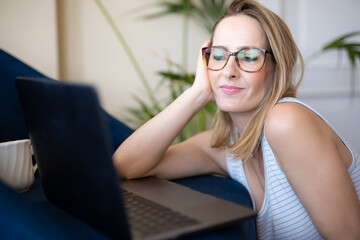 Attractive young woman working on laptop and smiling while sitting on the floor at home