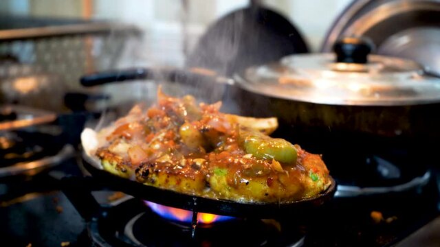 indian mixed vegatable dish sizzler with rice, fries, potato, vegetables cutlets and cabbage placed on iron dish being heated on a gas stove flame before serving the hot smoking dish
