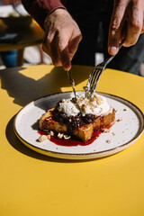 person eating dessert with brioche bread, cream, currant jam and nuts