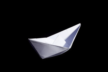 Top view of a white origami paper boat on black background.